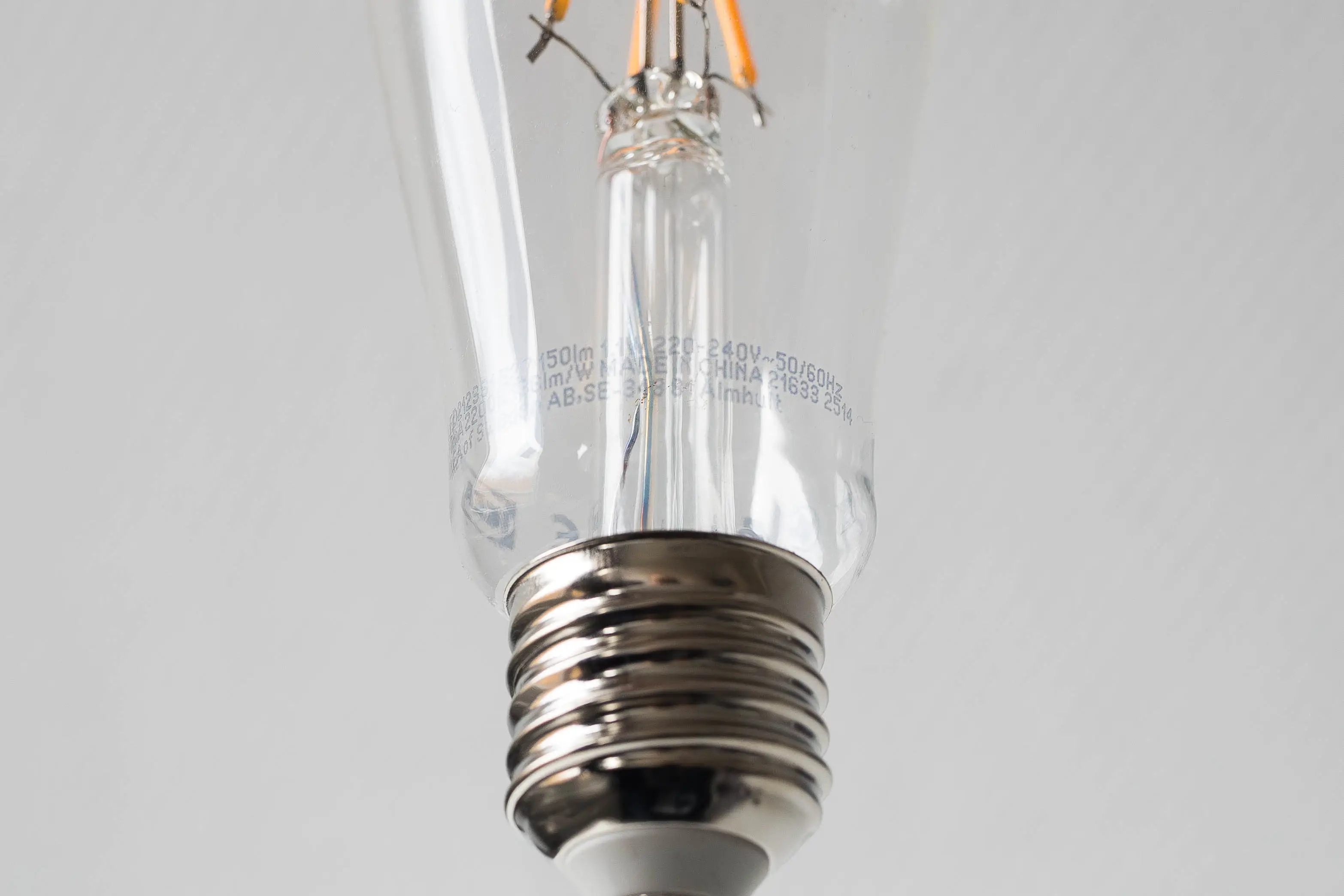 Close up shot of a lightbulb with an E27 thread, showing the description of the bulb containing wattage, lumen and volt.